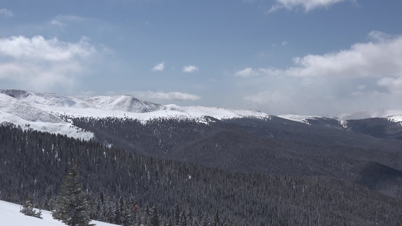 Opening view of Keystone, Colorado mountains with snow along the ridge, dark forest below, broken clouds overhead, and no visible people.
