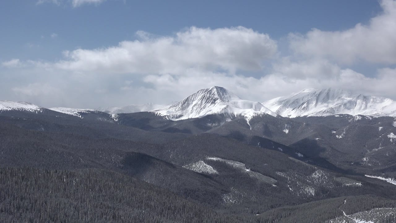 Distant snowy peaks over rolling winter forest hills