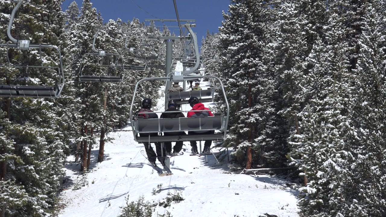Chairlift riders above a snowy slope between evergreen trees.