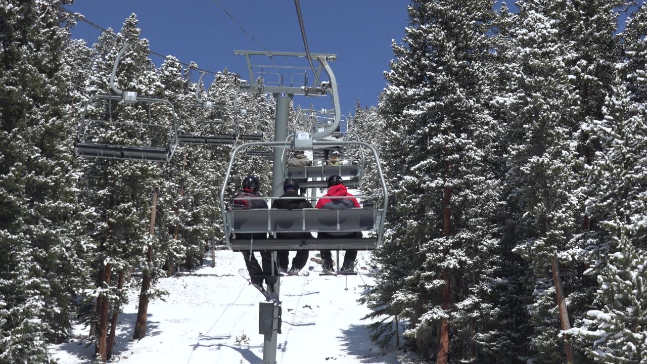 Chairlift riders above a snowy slope and evergreen trees.