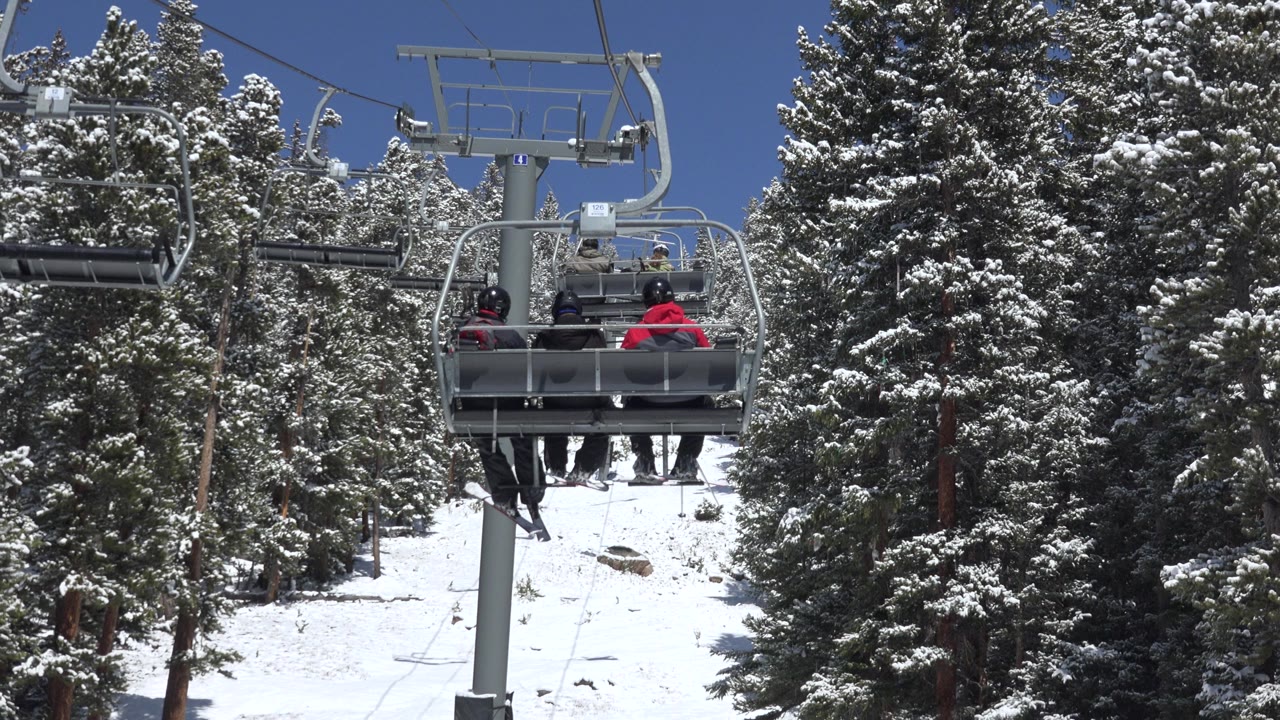 Three skiers ride a chairlift in Keystone, Colorado, with a lift tower, snow-covered pines, and blue sky visible at the start of the clip.