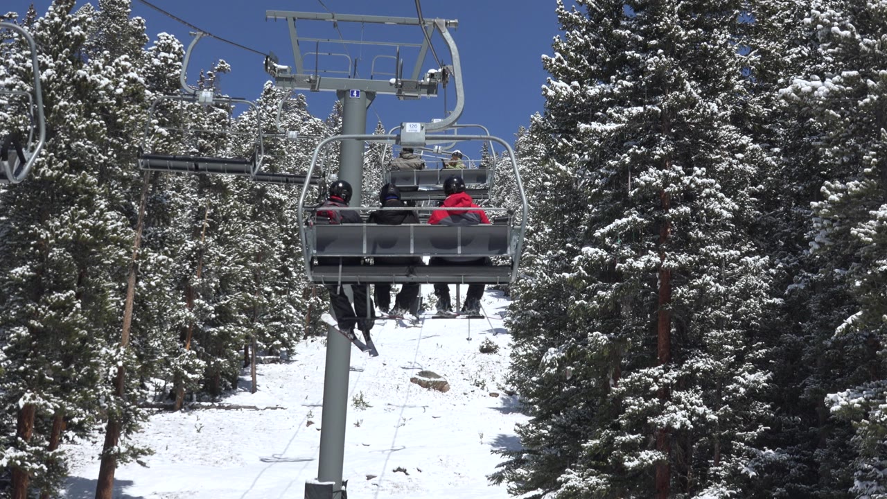 Skiers on chairlift framed by a support tower and pine forest