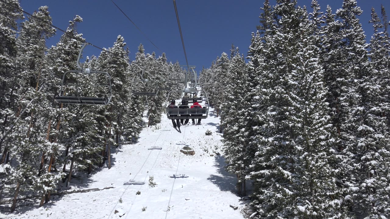 Snowy ski lift corridor with evergreen trees and chairlift cables.