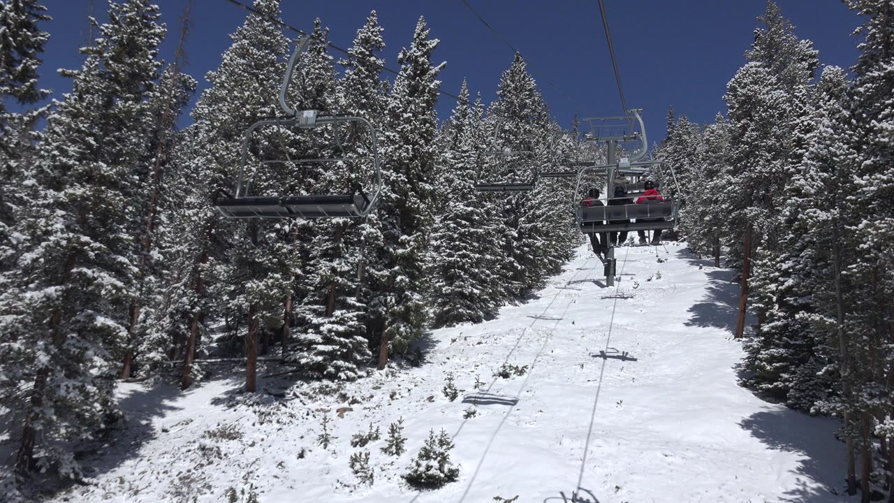 A Keystone, Colorado chairlift line runs up a snowy slope between dense evergreens, with a loaded chair near the upper right and no close faces visible.