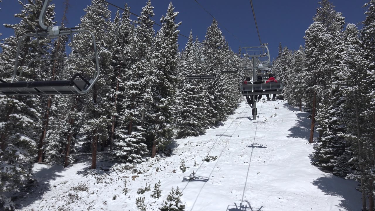 Empty chairlift seat passing over snowy evergreens
