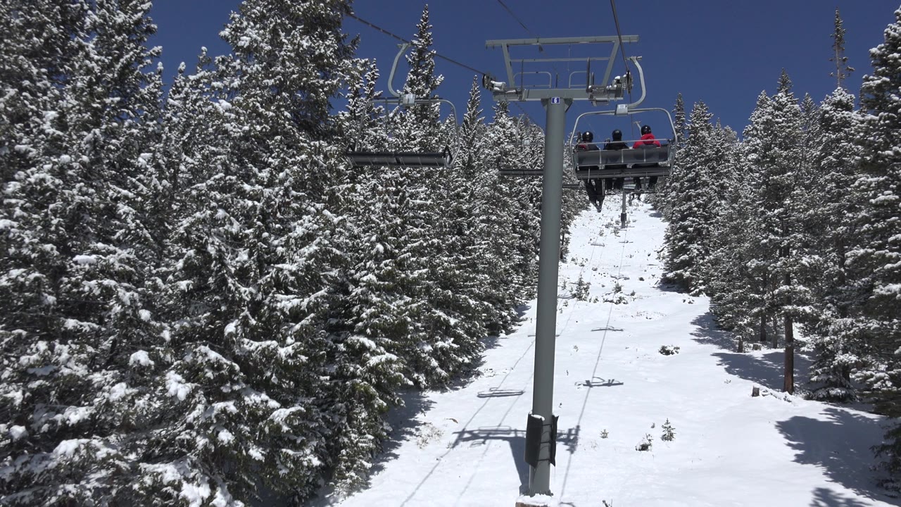 In Keystone, Colorado, a chairlift climbs between snow-covered evergreens under a clear blue sky, with a few riders visible near the upper center.