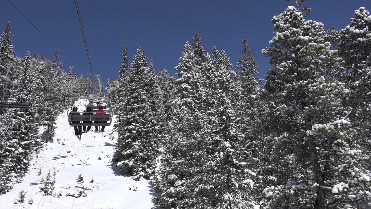 Chairlift with three people above a snowy forest slope.