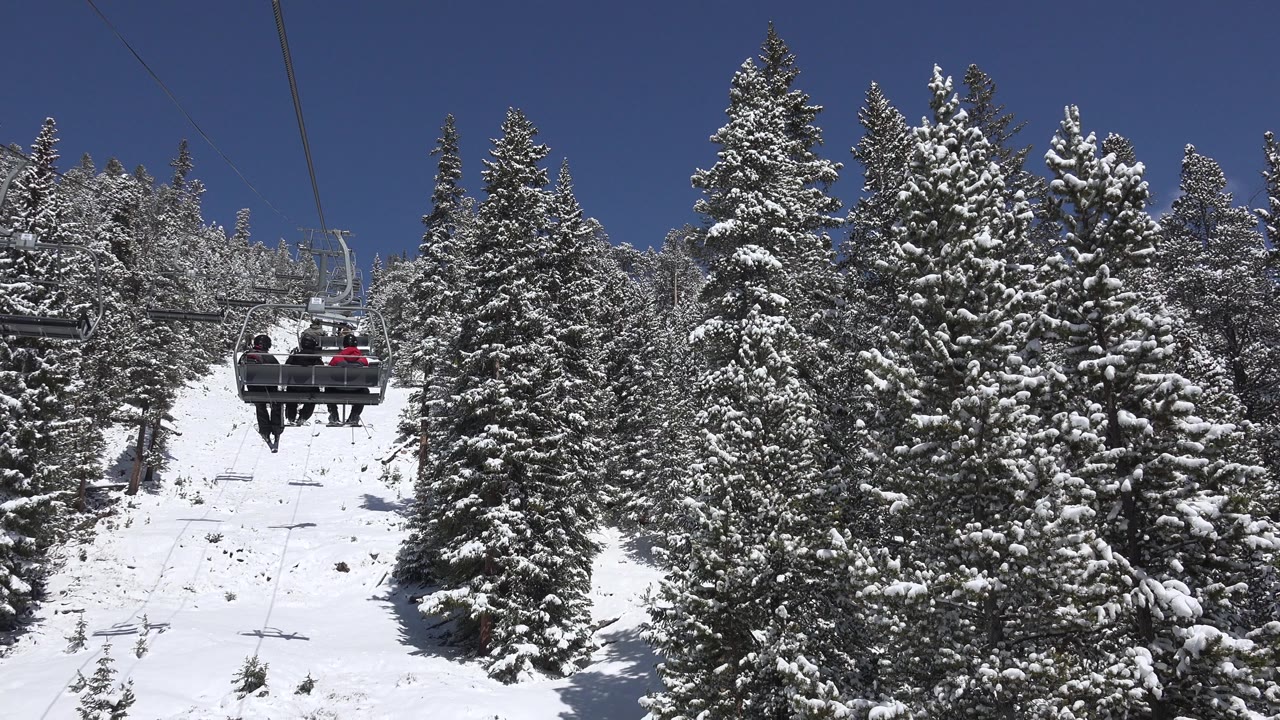 Chairlift riders above a snowy slope between evergreen trees.