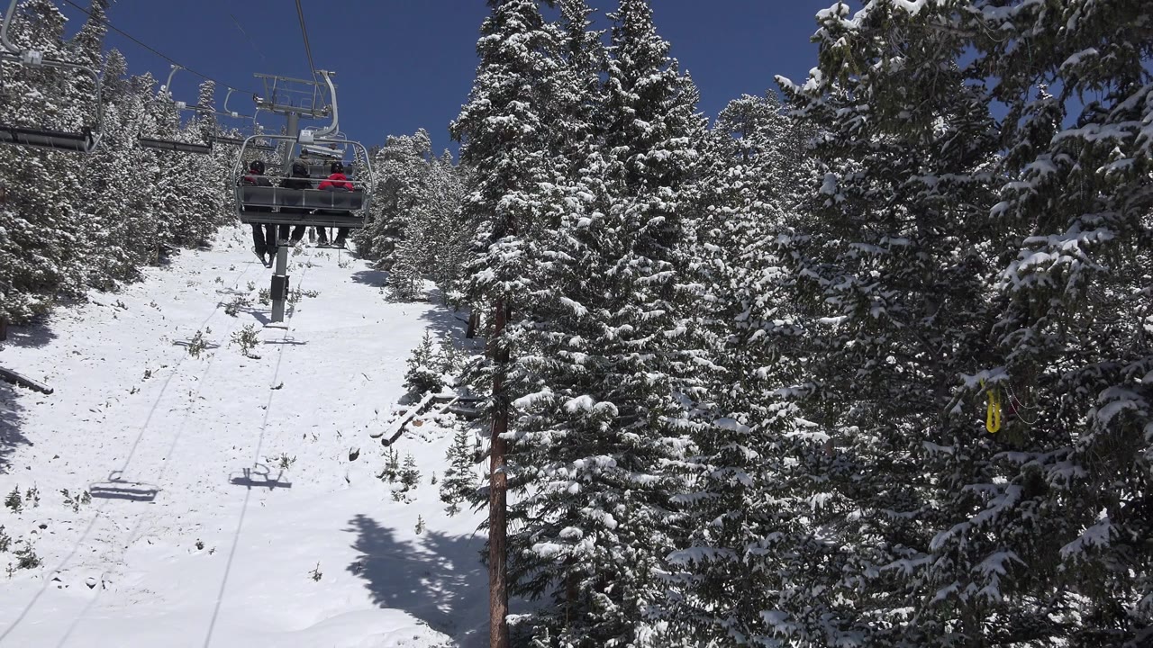 A Keystone, Colorado ski lift rises over a bright snowy run between tall snow-covered evergreens, with small distant riders on a chair near the top.