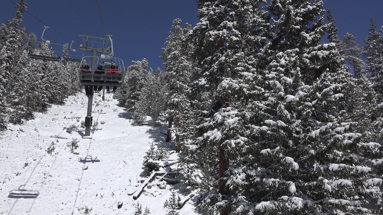 A ski lift chair with small riders appears near the upper center in Keystone, Colorado, with snow-laden evergreens filling the right side of the frame.