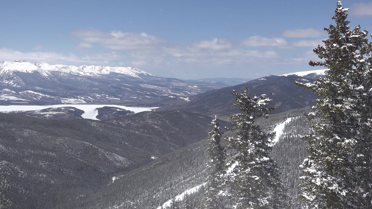 Snowy mountain valley with evergreen trees in the foreground.