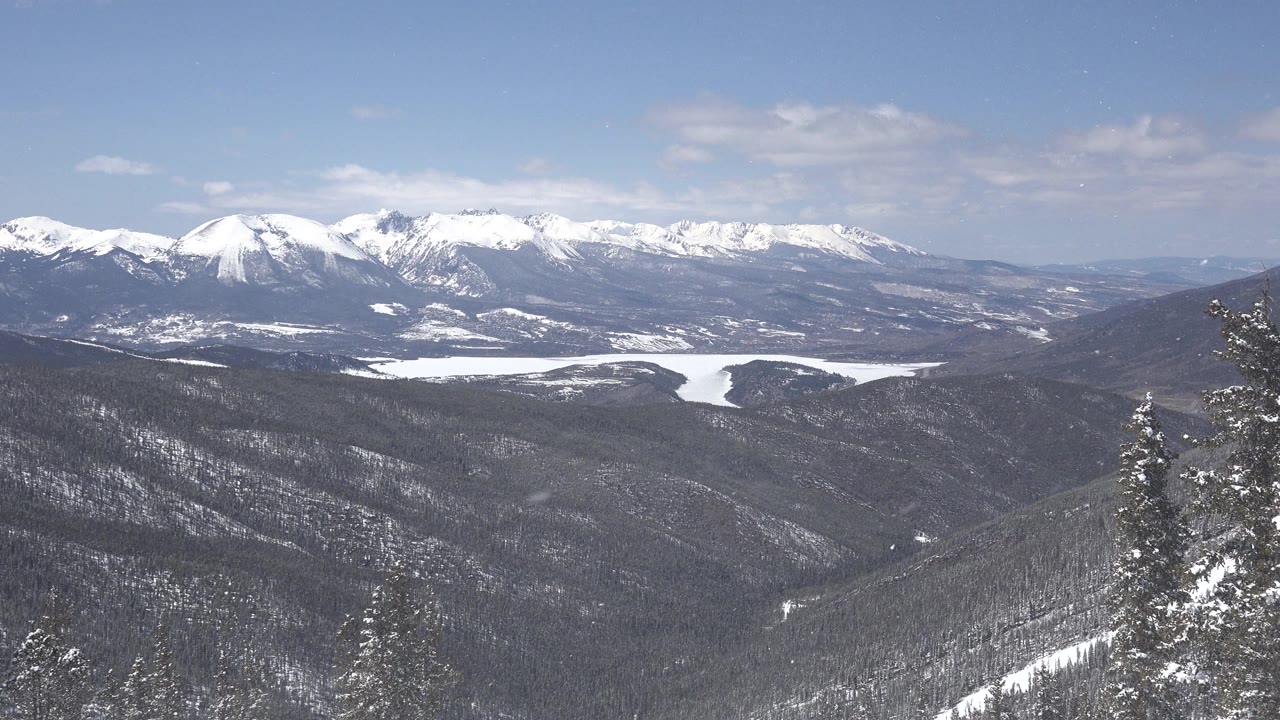 Wide view of snowy mountain ridges above a dark evergreen valley in Keystone, Colorado, with blue sky and no visible people.