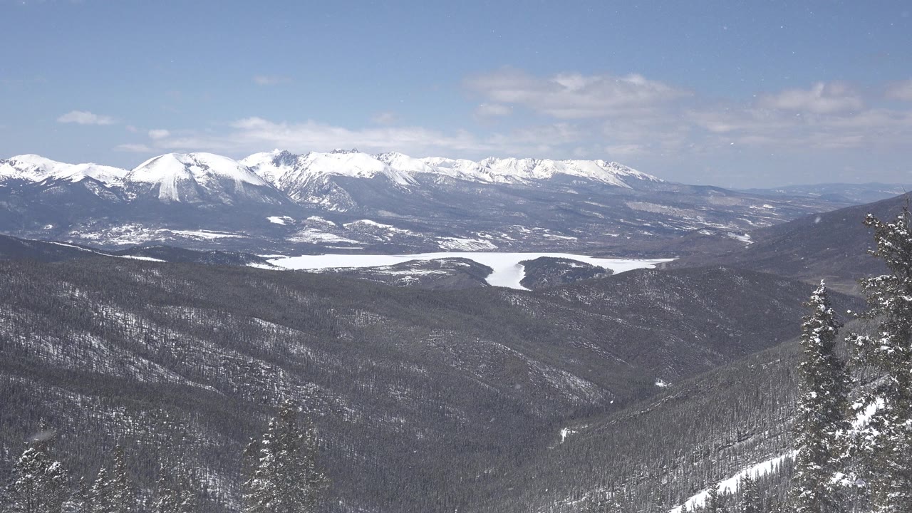 Keystone, Colorado winter panorama with snow-covered peaks, dark tree-covered hills, a pale frozen water shape, and no visible people.