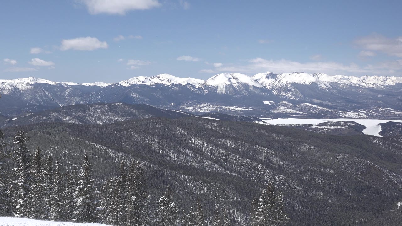 Wide Keystone, Colorado mountain view with snow-capped peaks, forested ridges, foreground evergreens, blue sky, and no visible people.