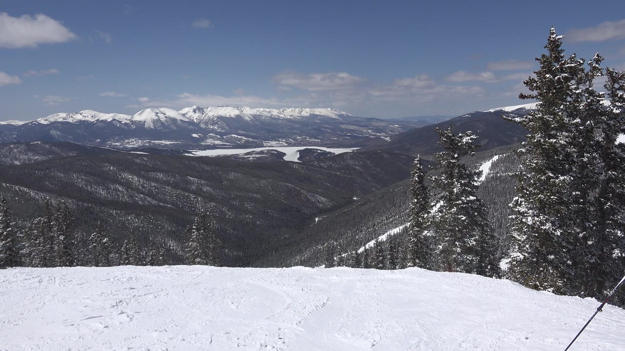 Wide Keystone, Colorado winter view from a snowy slope toward dark evergreen ridges and snow-capped mountains, with no visible people.