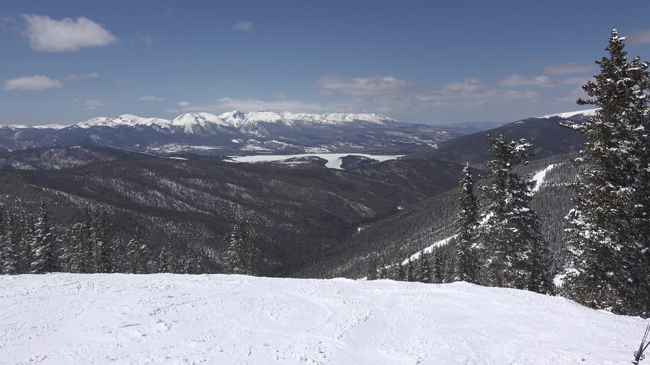 Mountain valley view with snowfield, trees, and blue sky