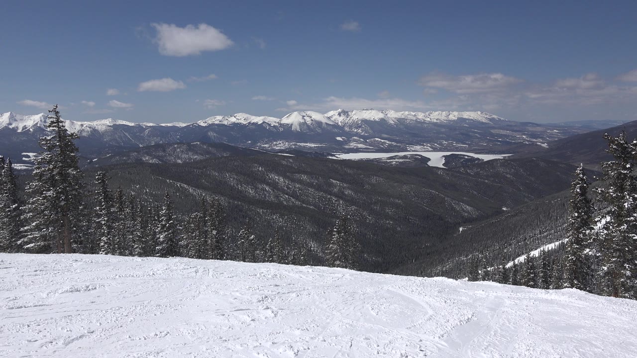 Wide Keystone, Colorado winter landscape with a snow-covered foreground slope, evergreen trees at the edges, distant mountain ridges, blue sky, and no visible people.