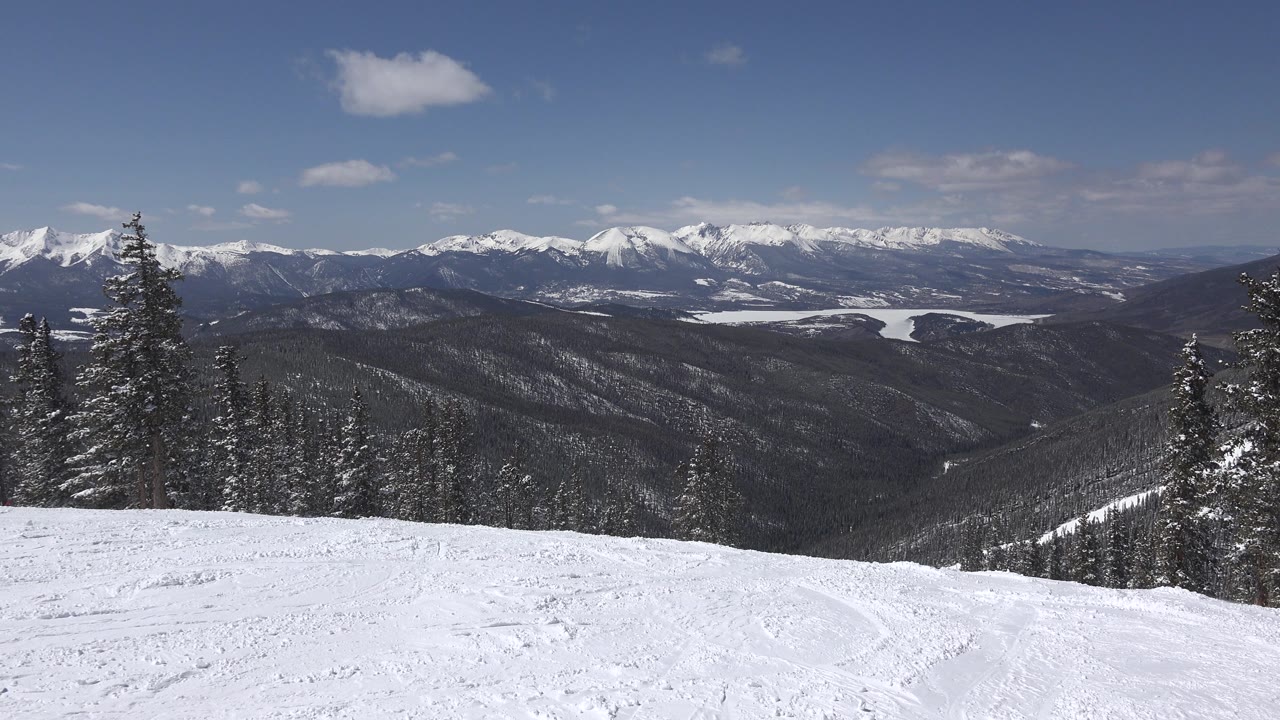 Wide snowy overlook with trees and a long mountain horizon.