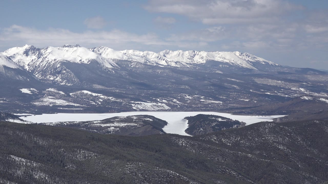 Alpine ridge with snowfields above a forested winter valley.