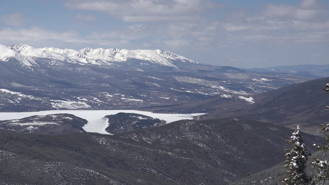 Wide snowy mountain panorama with forested slopes and distant peaks.