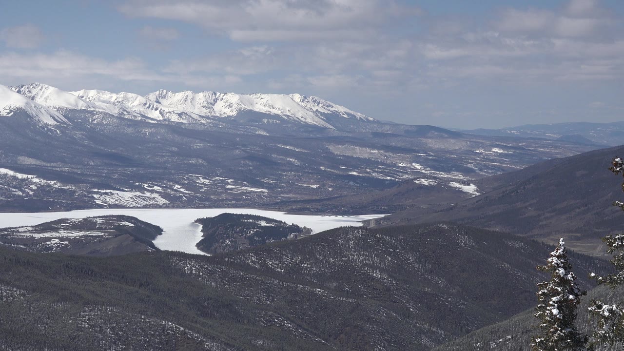 Keystone, Colorado mountain panorama with a white lake-like snowfield in the valley, dark ridges, distant snowy peaks, and no visible people.