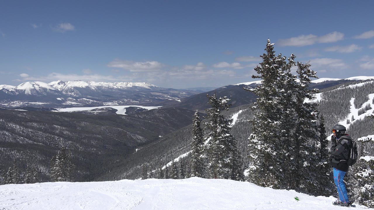 Keystone, Colorado mountain view with dark forested slopes, bright snow in front, tall evergreens in the midground, and one bundled adult facing the distant ridges.