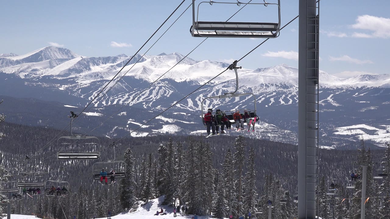 Chairlifts over snowy trees with mountains behind.