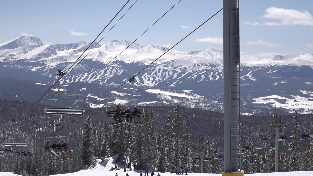 Chairlift riders with ski slopes and snowy mountains in the distance.