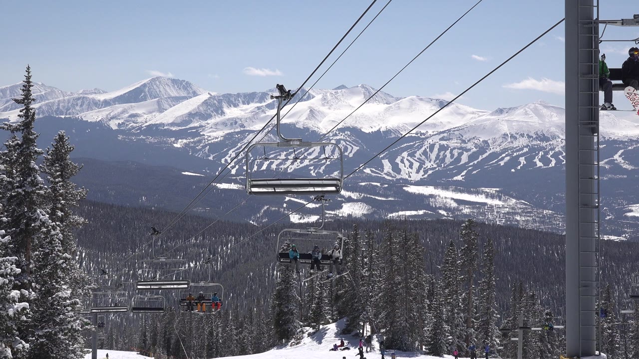 Ski lift chairs over snowy trees with mountains in the background.