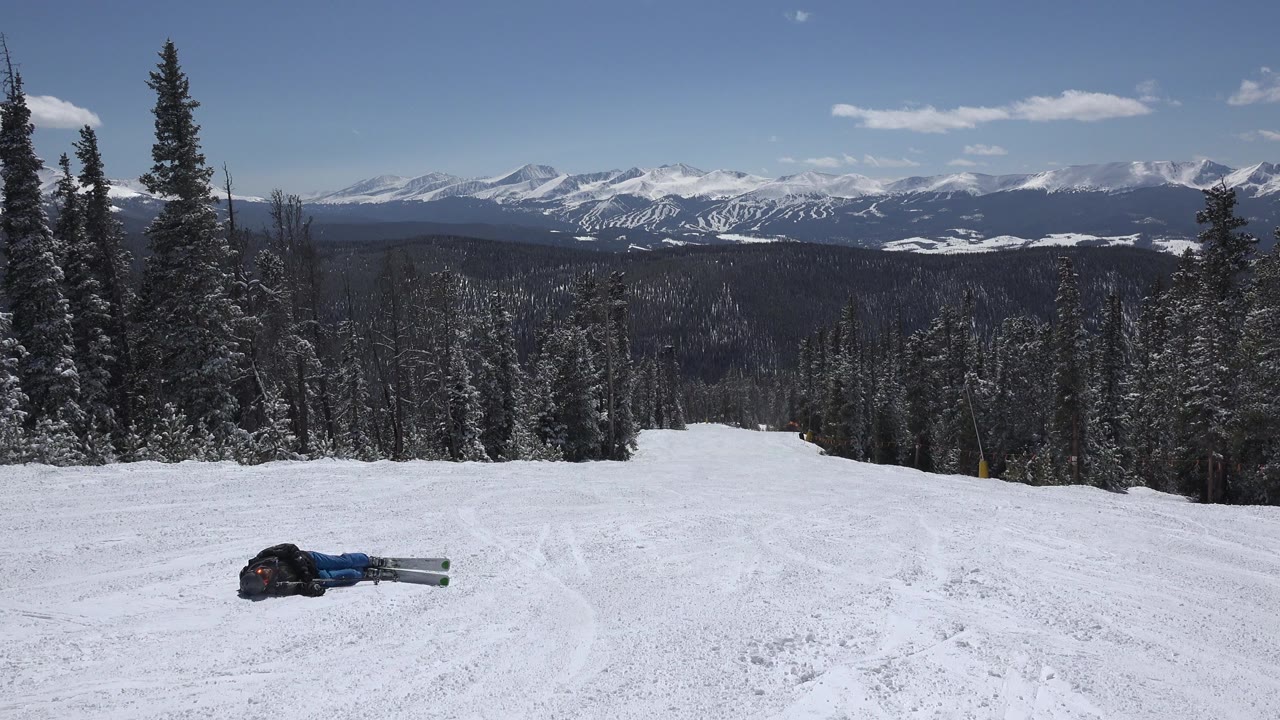 Person down on a snowy ski slope with mountains beyond.
