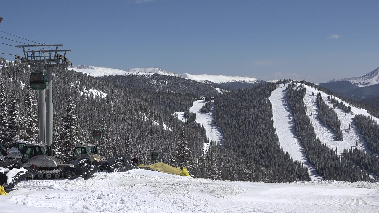 Keystone, Colorado ski area view with a lift tower on the left, gondola cabins above the snow, forested runs in the background, and no visible people.