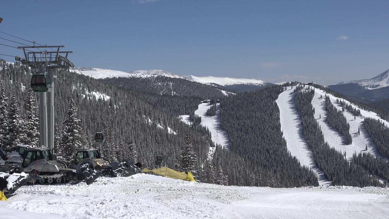 A Keystone, Colorado winter slope view shows gondola cabins near the left lift tower, groomed snow below, wooded mountain runs beyond, and no visible people.