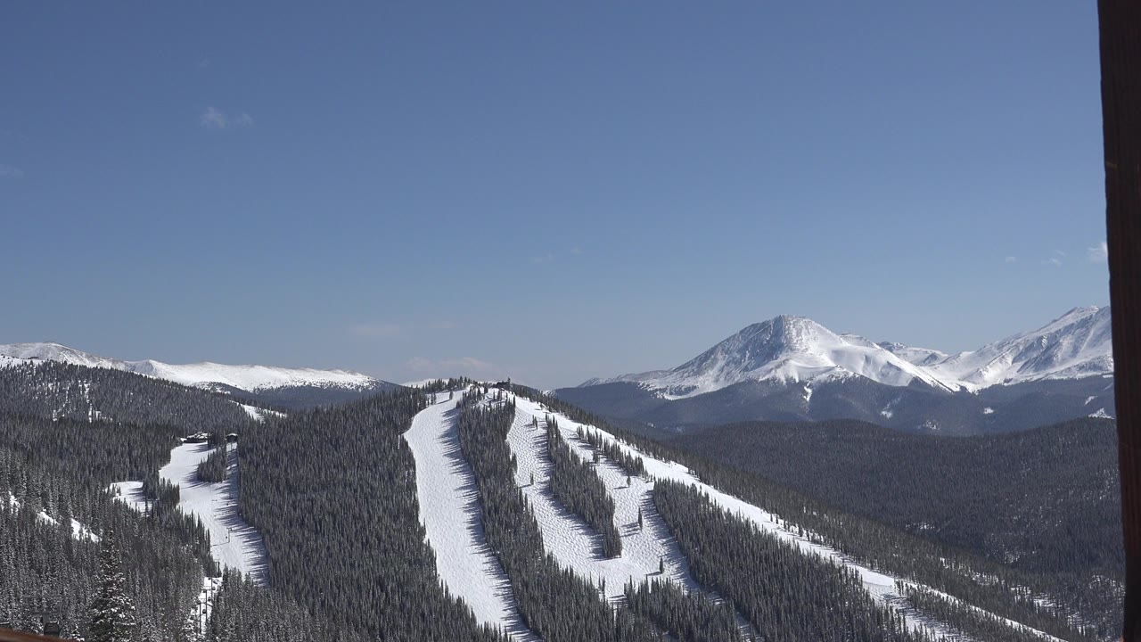 Wide Keystone, Colorado mountain view with snow-covered ski runs, dark evergreen forest, distant white peaks, clear blue sky, and no visible people.