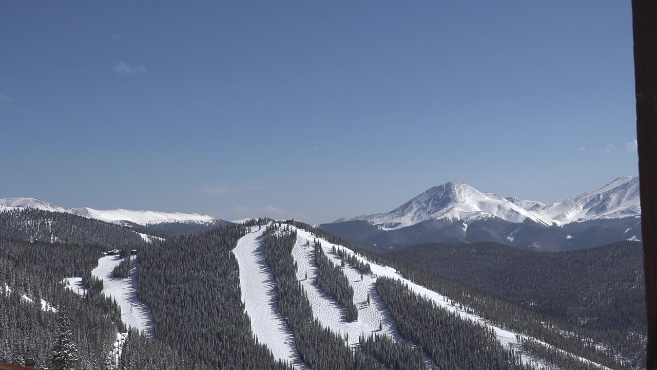 Keystone, Colorado landscape frame showing ski trails descending through evergreen trees toward a broad range of snow-covered mountains, with no visible people.