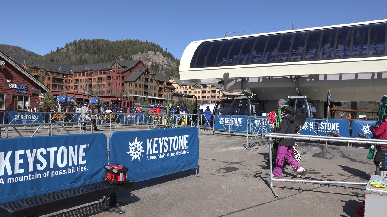 Snowboarders beside Keystone barriers at a chairlift base.