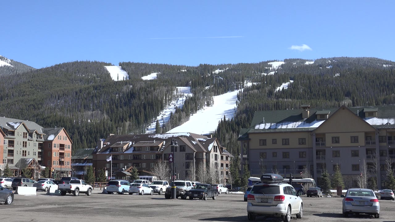 Wide resort base view with parking lot, buildings, trees, and ski runs.