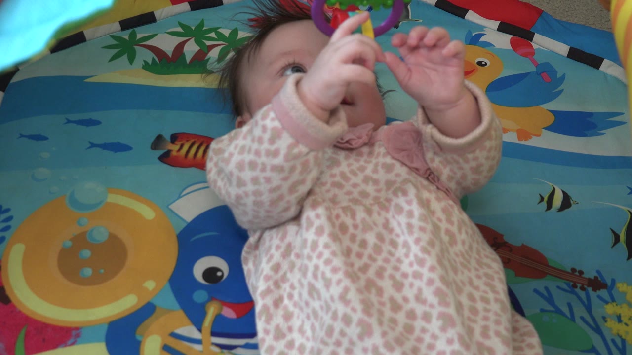 Baby lying on a colorful fish play mat and reaching upward.