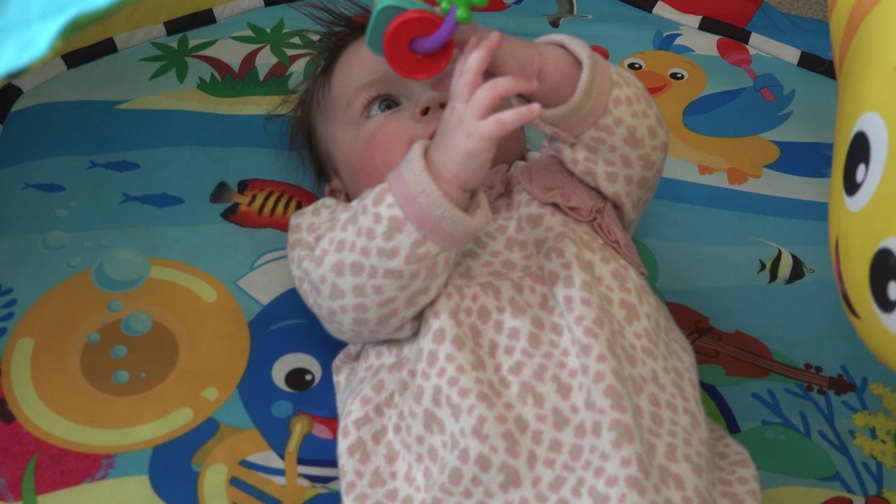 Newborn looks at a colorful hanging toy above the play mat.
