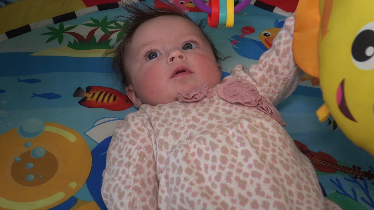 Baby lying on a colorful play mat beneath hanging toys.