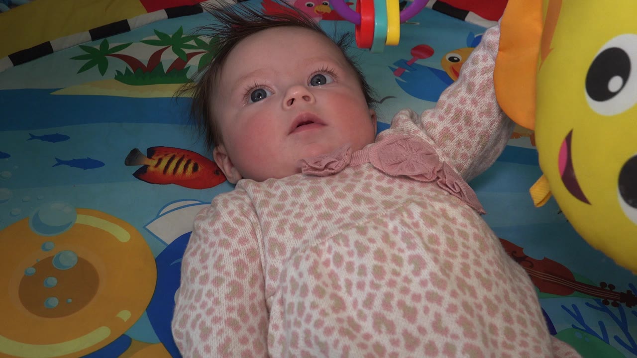 The baby remains on the activity mat in Westminster, Colorado, with a large yellow hanging toy close to the right edge and ocean-themed graphics behind.