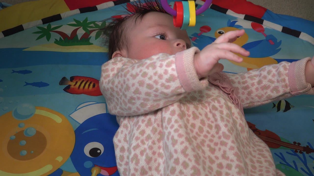 Baby lying on a colorful play mat reaching upward.