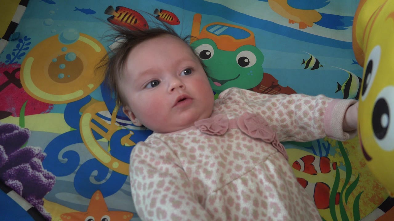 In Westminster, Colorado, a baby in a pale patterned onesie lies on an ocean-themed mat while a yellow fish-shaped balloon is cropped along the right edge.