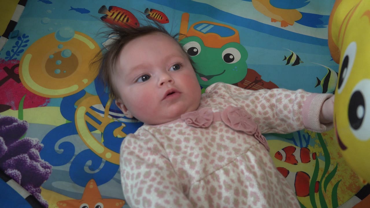 In Westminster, Colorado, the baby remains on the ocean-patterned mat and looks toward the large yellow fish balloon at the right side of the frame.