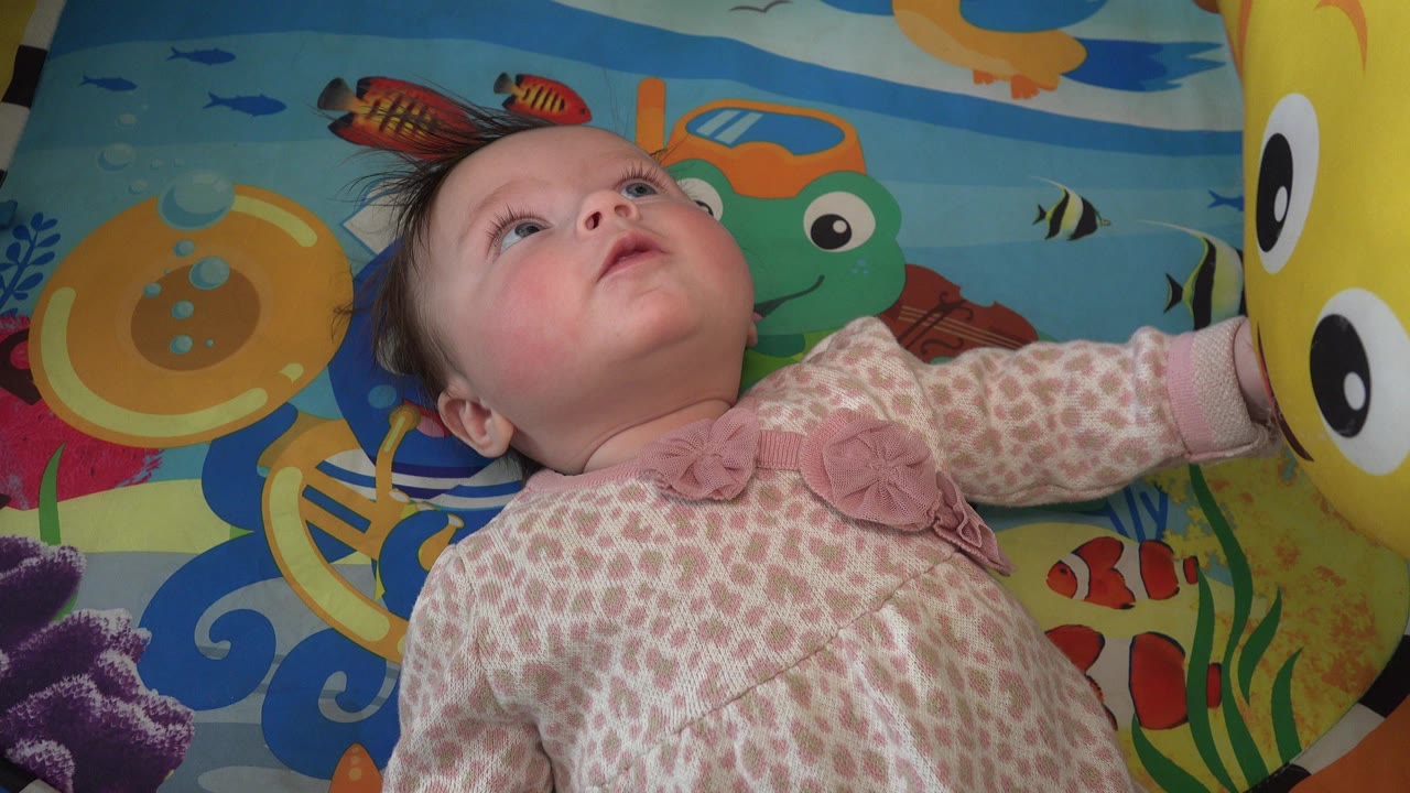 A baby in Westminster, Colorado lies on a sea-themed play mat, looking upward while a yellow happy-face balloon fills the right edge of the frame.