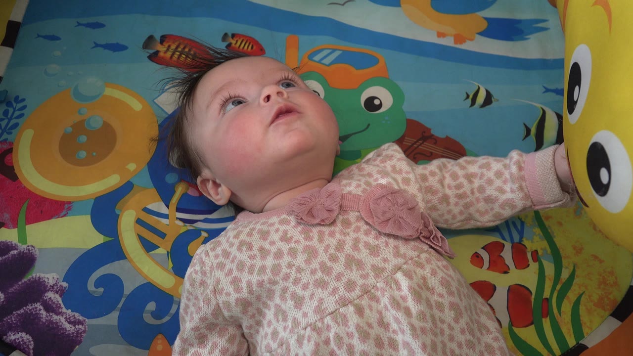 The baby remains on the illustrated play mat in Westminster, Colorado, eyes lifted toward the yellow happy-face balloon partly visible at the right edge.
