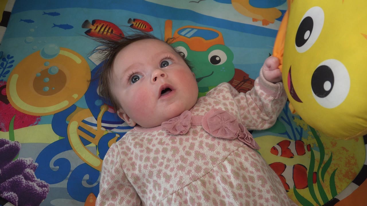 Baby looking at a large yellow happy-face balloon on a colorful mat.