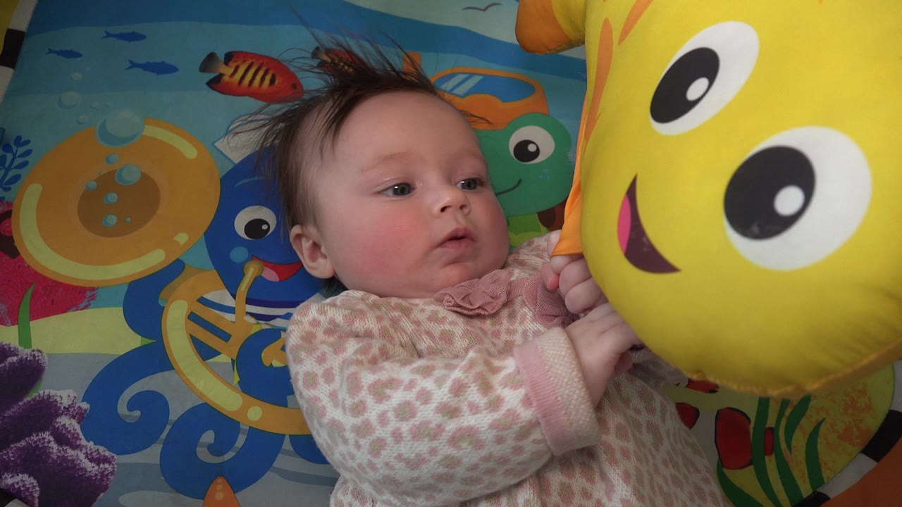 Baby lying on a colorful play mat beside a yellow smiling toy.