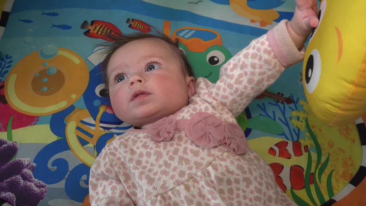 Baby girl lying on a colorful play mat and looking upward.
