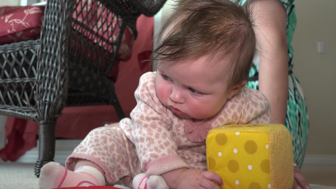 Infant seated on carpet beside a yellow plush cheese toy.