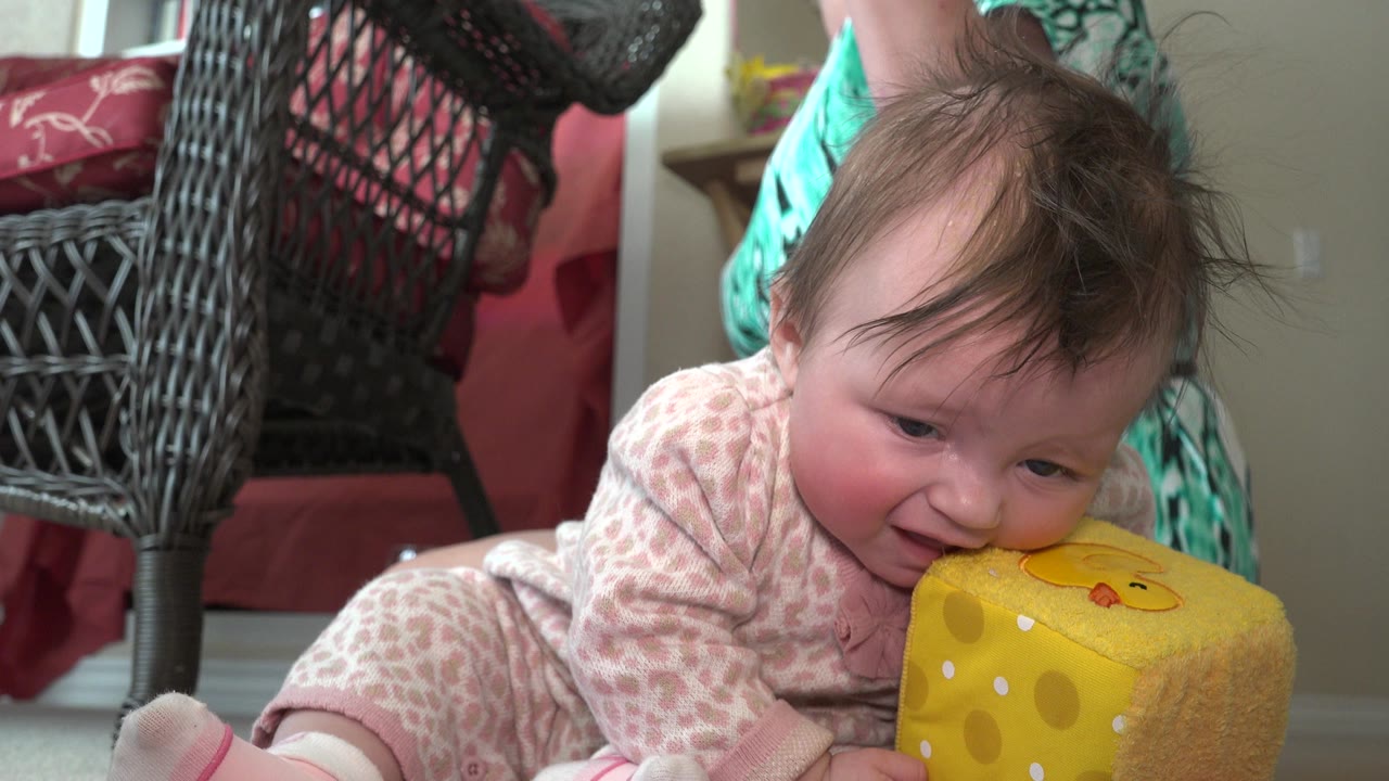 Baby on carpet leaning toward a yellow soft cube.